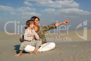 happy mother and daughter sitting on sand family scene