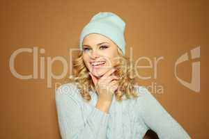 Gorgeous young woman with blond ringlets in a green knitted winter outfit ,over light brown