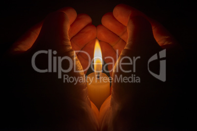 Protective hands around a burning candle.