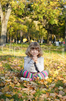 beautiful little girl sitting on autumn leaves in park