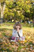 beautiful little girl sitting on autumn leaves in park