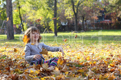 happy little girl throws autumn leaves