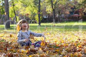 happy little girl throws autumn leaves