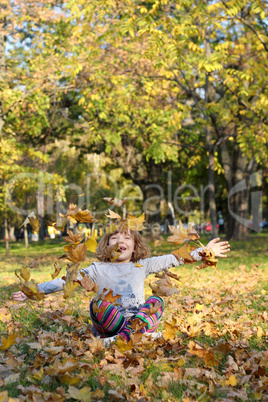 beautiful little girl throws autumn leaves