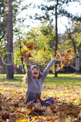 happy little girl throws leaves