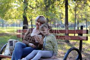 mother and daughter sitting in park and play with tablet