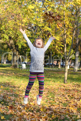 little girl jump and throws leaves