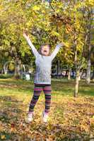 little girl jump and throws leaves