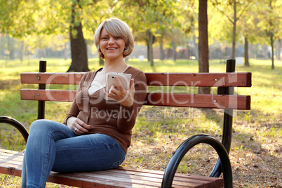 beautiful woman sitting in park and play with tablet