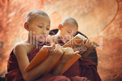 Young Buddhist novice monks reading outside temple