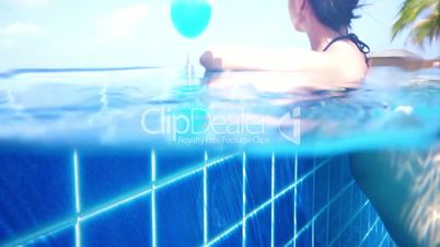 Girl looking at the ocean while sitting by the pool - camera begin to shooting underwater and coming out.