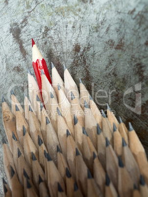 Close up of identical graphite pencils and one red leading crayo