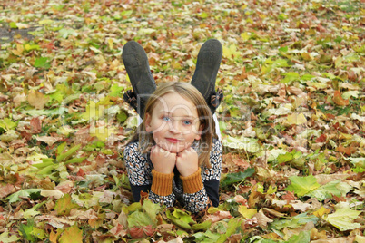 little girl lays on the ground in the Autumn park