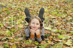 little girl lays on the ground in the Autumn park