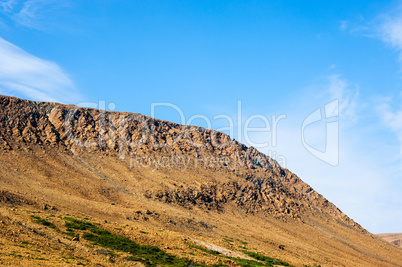 Rocky dry yellow cliff slope against light blue sky