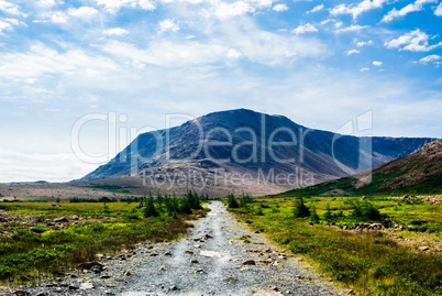Rocky gravel path leading to mountain under clouds and sky