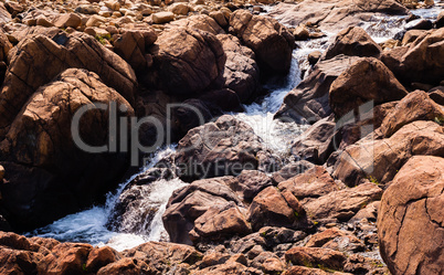 Stream flowing and splashing among bare red rocks