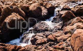 Stream flowing and splashing among bare red rocks