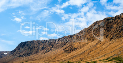 Rocky dry yellow cliff slope against light blue sky