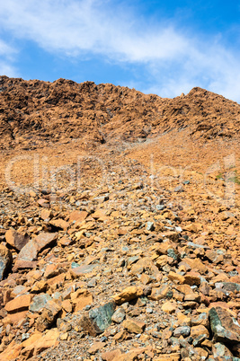 Dry yellow broken rocks on mountain slope against sky