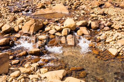 Clear shallow water flowing and splashing on bare rocks