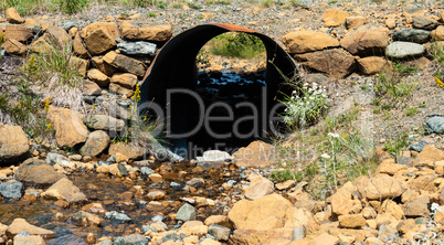 Looking through rusted corrugated metal pipe in rocky ground