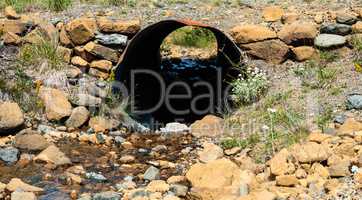 Looking through rusted corrugated metal pipe in rocky ground