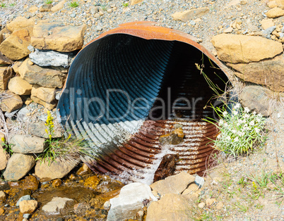 Rusted corrugated metal pipe in rocky ground