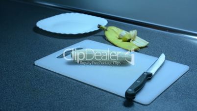 Cutting a banana into slices and inserting on the plate on the kitchen counter