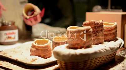 Trdelník (chimney cake or stove cake) in shop (in night) - man in the background spread cake with hazelnut cream