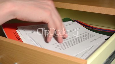 hand (young man) takes some papers from the desk drawer