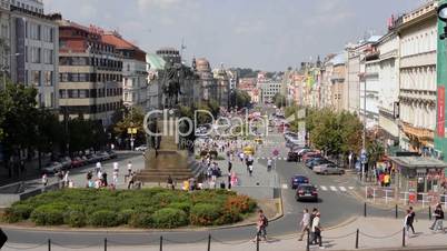 Wenceslas Square with people and passing cars - buildings and nature(trees and bushes) - blue sky