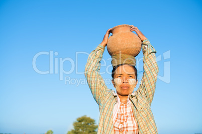 Mature Asian traditional female farmer carrying clay pot on head