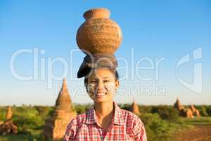 Young Asian traditional female farmer carrying clay pot on head