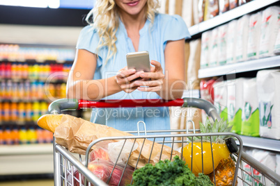 Smiling woman with cart using smartphone