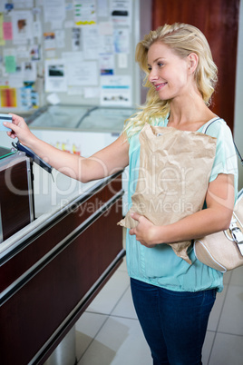 Smiling woman paying with credit card and holding grocery bag