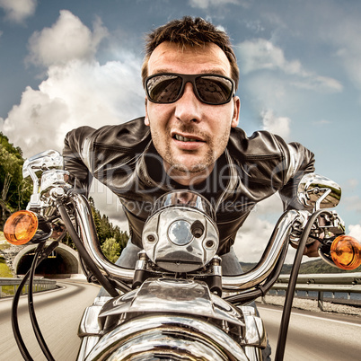 Funny Biker in sunglasses and leather jacket racing on mountain