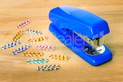 Stapler of bright blue color and paper clip against a table.