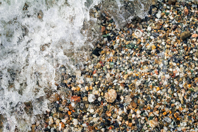 Small sea stones on the seashore, covered with a sea wave.