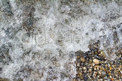 Small sea stones on the seashore, covered with a sea wave.