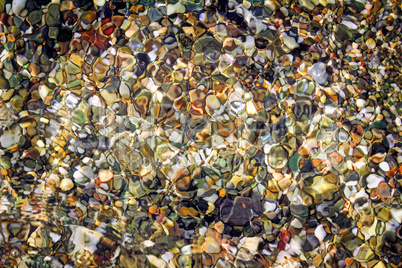 Small sea stones on the seashore, covered with a sea wave.