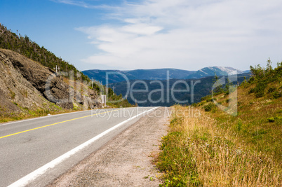 Empty paved road and gravel shoulder against hills and mountains