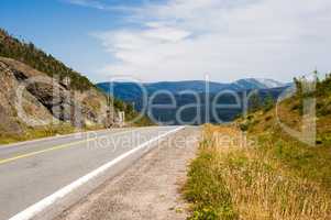 Empty paved road and gravel shoulder against hills and mountains