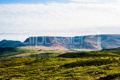 Green hills with forest against plateau under cloudy sky