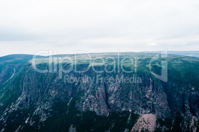 Large steep cliffs and plateau under overcast sky and fog