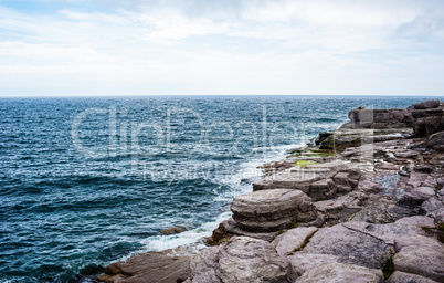 Horizon and rocky coastline with waves splashing under cloudy sk