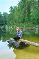 beautiful girl sits on the log by the river