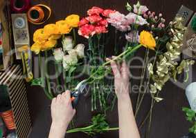 Florist cutting yellow flower on brown wooden table, top view