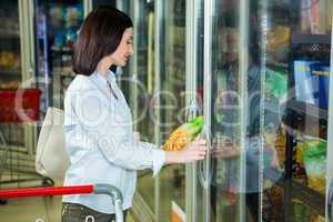 Smiling woman picking chips package in fridge