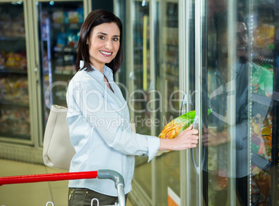 Smiling woman picking chips package in fridge